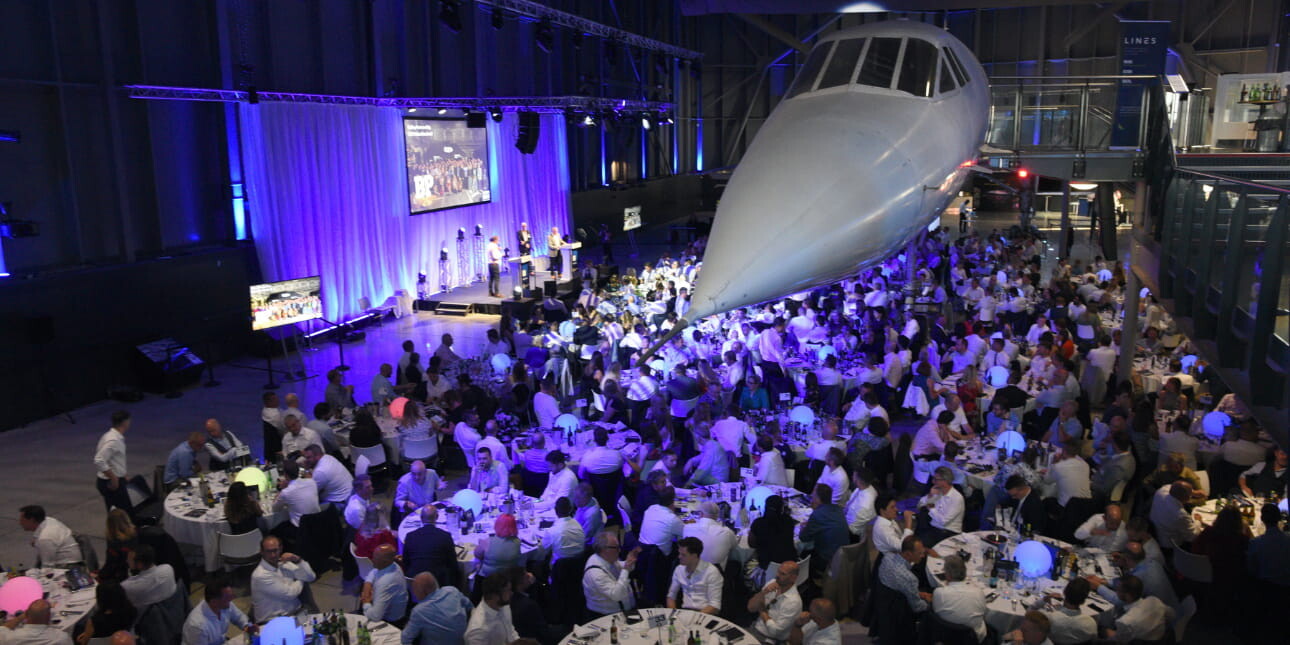 Arial shot of an awards ceremony with tables and chairs and a stage placed under a Concorde plane